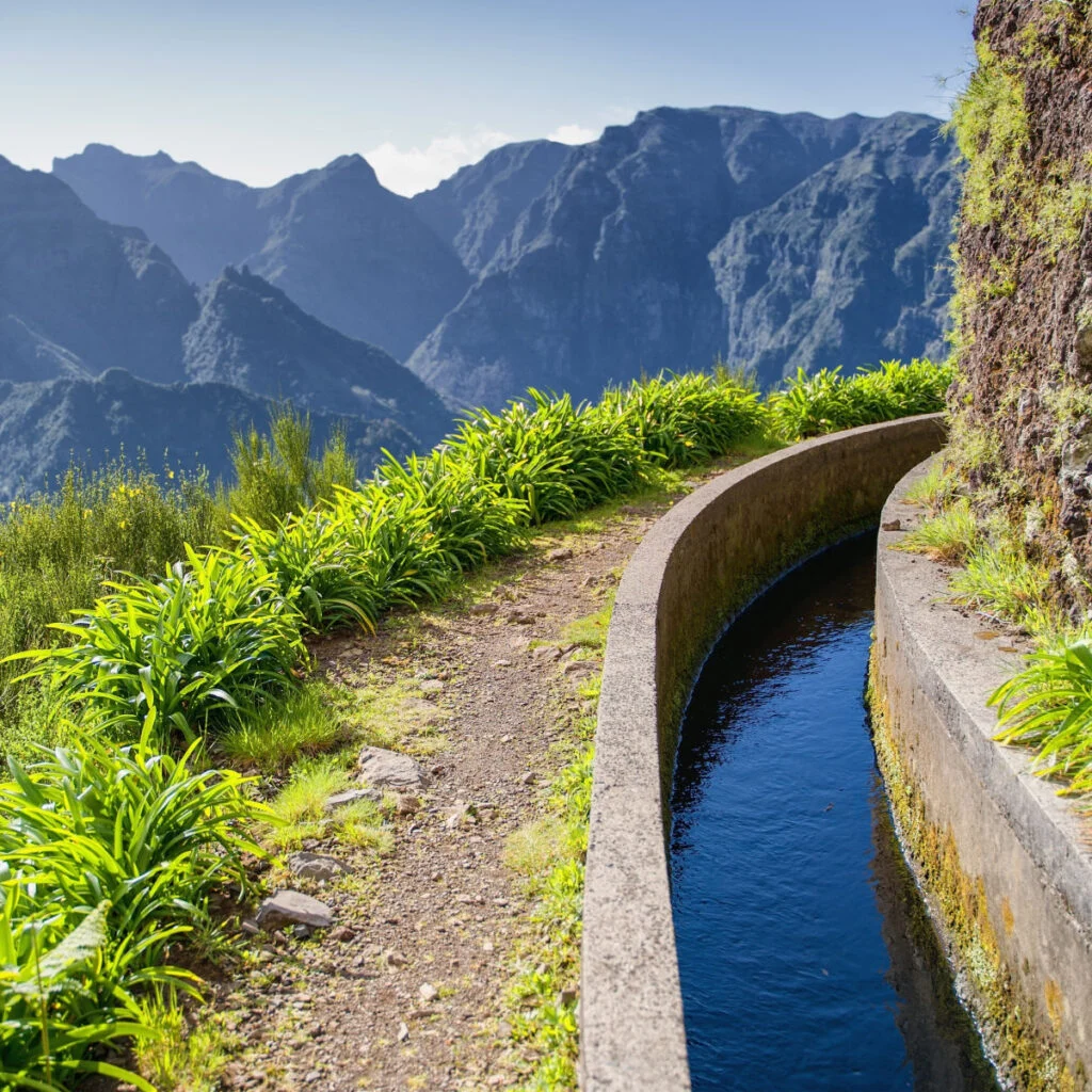 View from Levada do Norte on the portuguese island of Madeira. Spring in Madeira. Levada irrigation canal. Hiking in Madeira. Narrow path next to the levada. Green mountains in background.