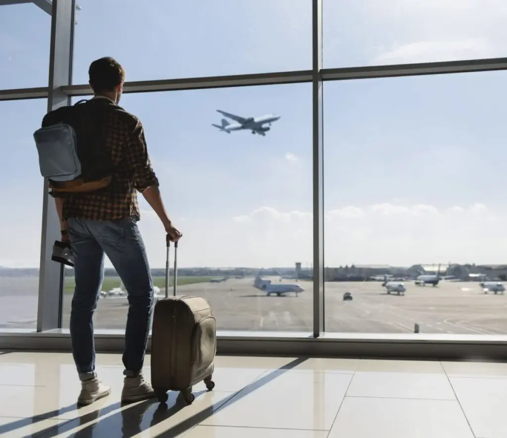 Young man near window at the airport watching plane before departure.